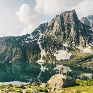 person standing on rock near lake and mountain range