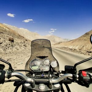 a motorcycle driving down a desert road with mountains in the background
