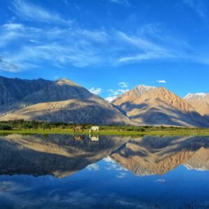 green and brown mountains beside lake under blue sky during daytime